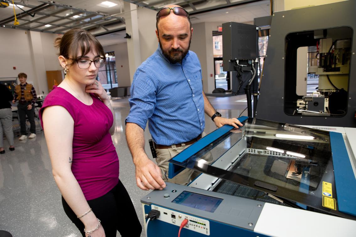 SEED Director Evan Jones assists Megan Brown ’26 with using a laser cutter to make earrings she designed